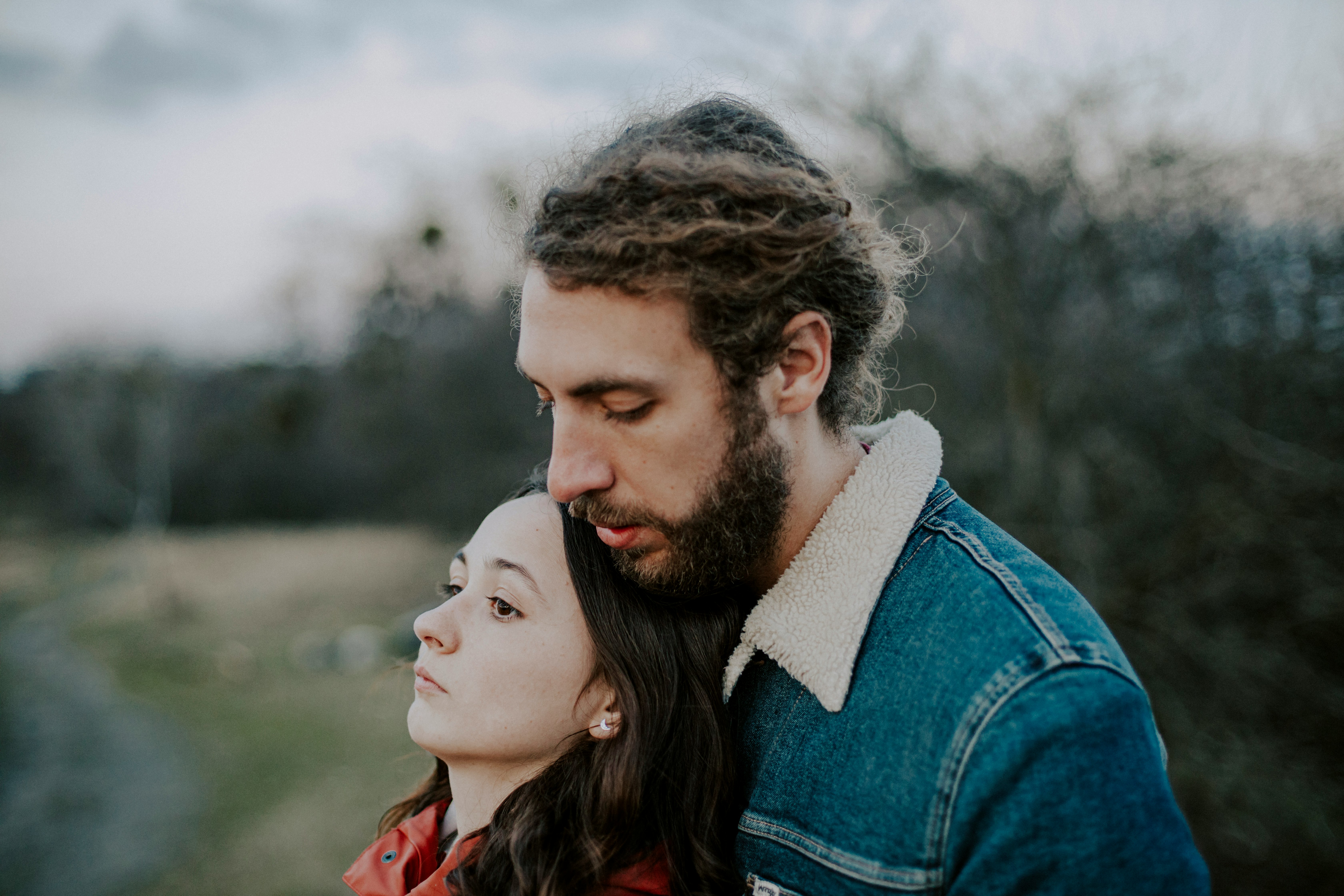 man in blue denim jacket kissing woman in red and black plaid shirt